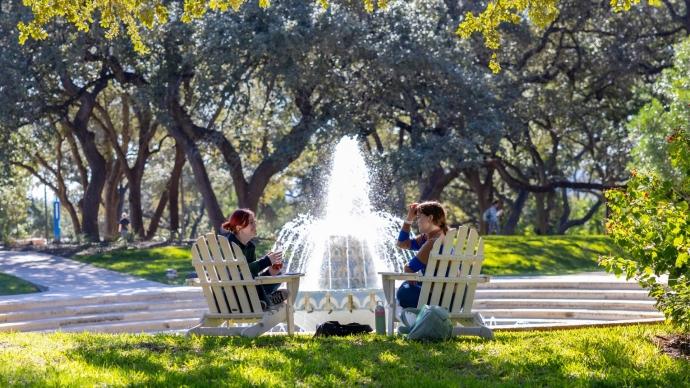 Two students sit in Adirondack chairs in front of Miller Fountain